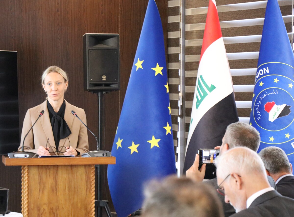 A person standing at a podium with flags behind her

Description automatically generated